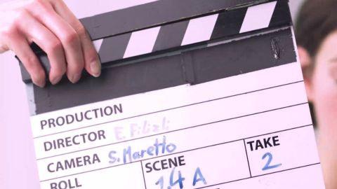 Filmklappe bei einer VUCX Videoproduktion mit Regie- und Kamera-Angaben, gehalten von einer Hand am Set